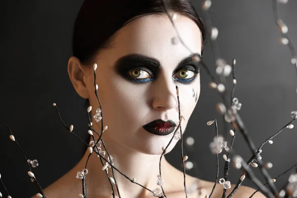 Schöne Frau mit Halloween-Make-up und Zweigen auf dunklem Hintergrund — Stockfoto