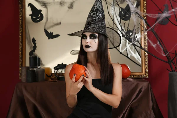 Mulher bonita vestida de bruxa no quarto decorado para o Halloween — Fotografia de Stock