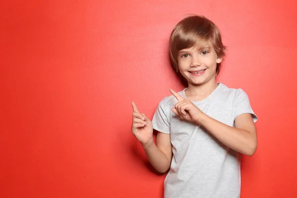 Little boy in t-shirt pointing at something on color background — Stock Photo, Image