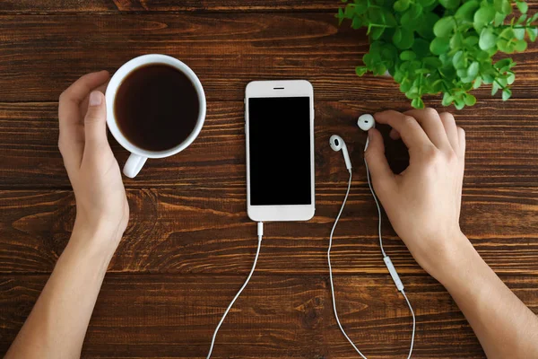 Mains féminines avec tasse de thé, téléphone portable et écouteurs sur fond en bois, vue de dessus — Photo