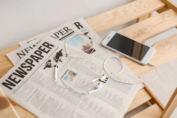 Teléfono móvil con auriculares y periódicos en estante de madera — Foto de Stock