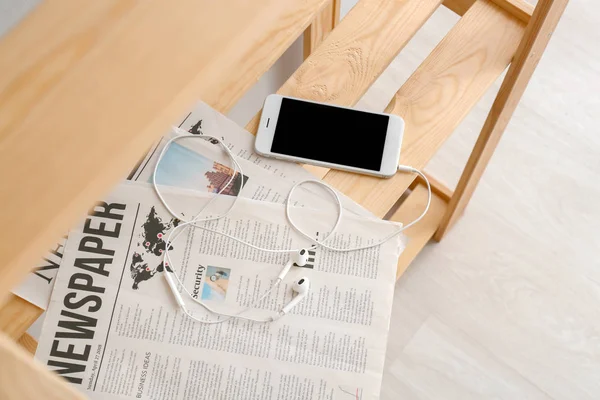 Teléfono móvil con auriculares y periódicos en estante de madera — Foto de Stock