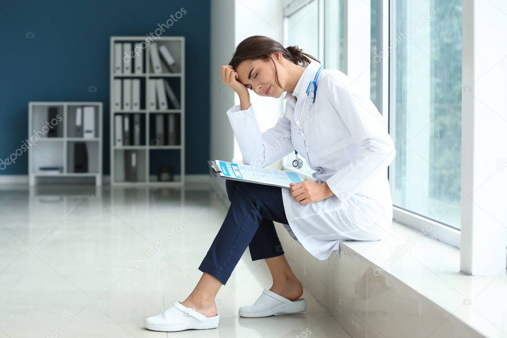 Tired female doctor sitting on windowsill in her office