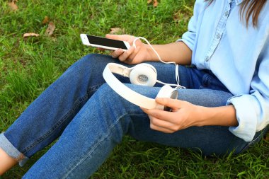 Hareket eden telefon ve kulaklık yeşil çimenlerin üzerinde oturan genç kadınla