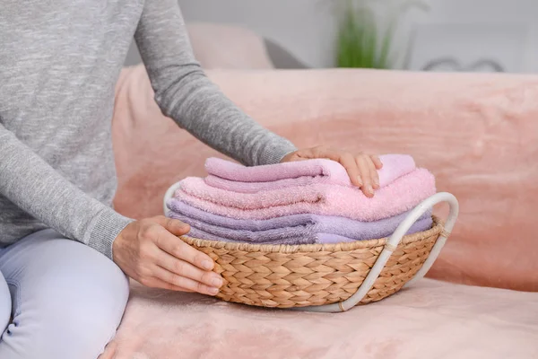Mulher dobrar toalhas macias limpas em cesta de vime no sofá em casa — Fotografia de Stock