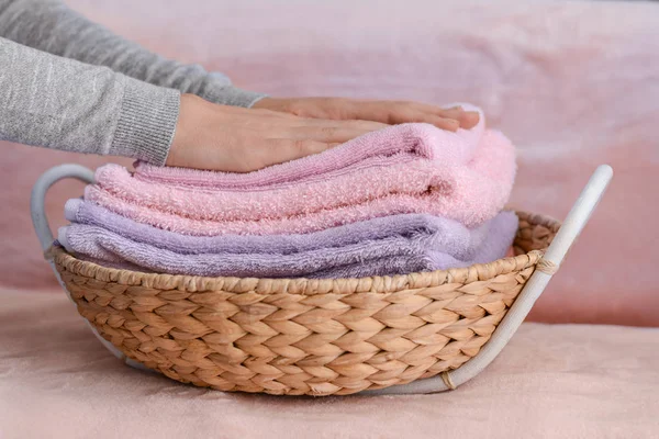 Mulher dobrar toalhas macias limpas em cesta de vime no sofá em casa — Fotografia de Stock