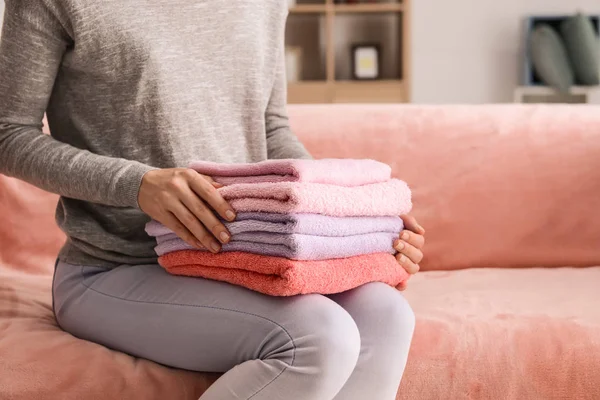 Женщина со стопкой чистых мягких полотенец на диване дома — стоковое фото