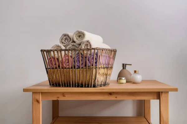 Cesta com toalhas limpas e macias e cosméticos em mesa de madeira — Fotografia de Stock
