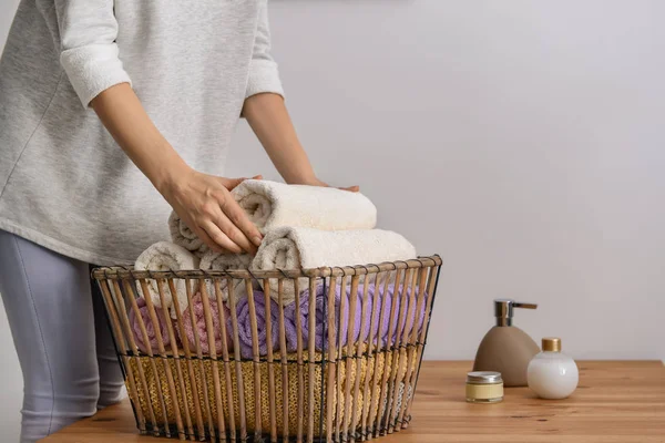 Woman folding clean soft towels into basket at wooden table — Stock Photo, Image