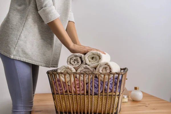 Woman folding clean soft towels into basket at wooden table — Stock Photo, Image