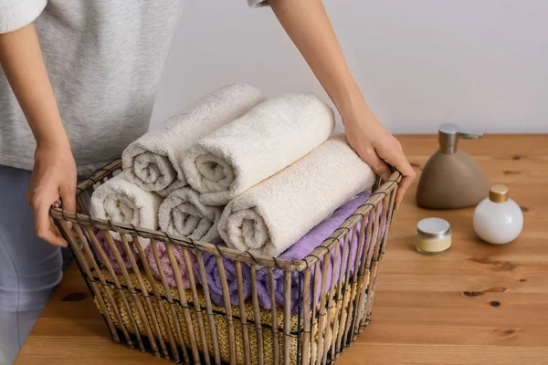 Mulher dobrando toalhas macias limpas em cesta na mesa de madeira — Fotografia de Stock