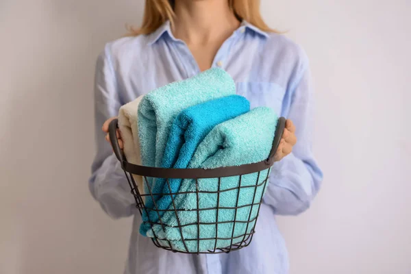 Vrouw met metalen mand met schone zachte handdoeken op lichte achtergrond — Stockfoto