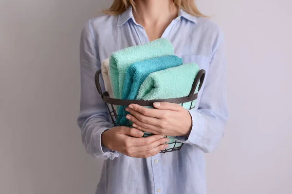 Vrouw met metalen mand met schone zachte handdoeken op lichte achtergrond — Stockfoto