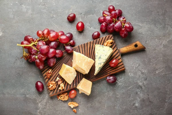 Placa de madeira com queijo, uvas suculentas maduras e nozes na mesa cinzenta — Fotografia de Stock