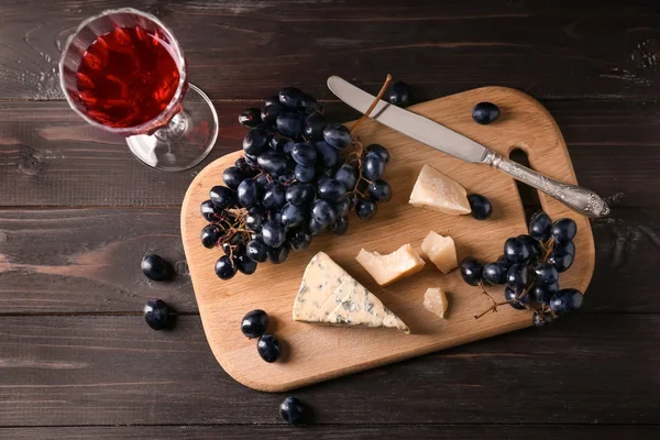 Бокал красного вина с сыром и свежим виноградом на деревянном столе — стоковое фото