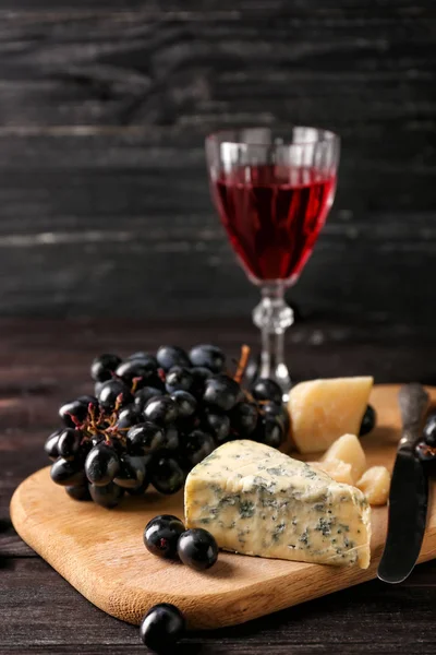 Uvas frescas con queso y copa de vino tinto sobre tabla de madera — Foto de Stock