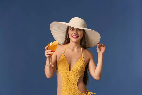 Beautiful woman in swimming suit and with tasty summer cocktail on color background — Stock Photo, Image