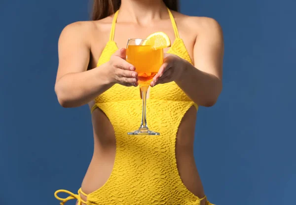 Beautiful woman in swimming suit and with tasty summer cocktail on color background — Stock Photo, Image