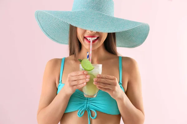 Beautiful woman in swimming suit and with tasty summer cocktail on color background — Stock Photo, Image