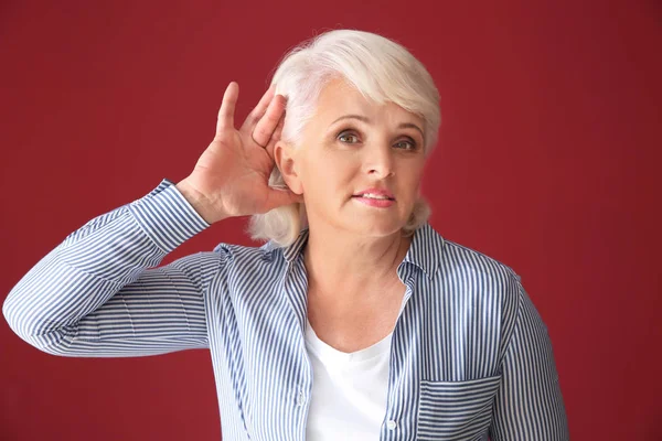 Portrait of mature woman trying to hear something on color background — Stock Photo, Image