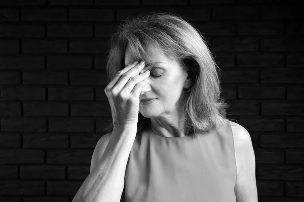 Retrato en blanco y negro de una mujer madura con dolor de cabeza sobre un fondo oscuro — Foto de Stock