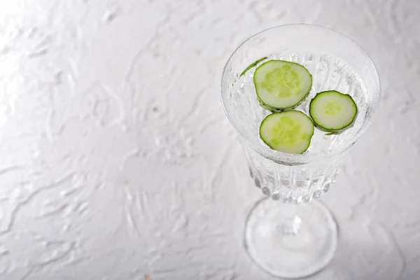 Glass of fresh cucumber water on white table