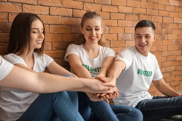 Team of young volunteers putting hands together indoors — Stock Photo, Image