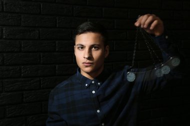 Male hypnotist with swinging pendulum on dark background clipart