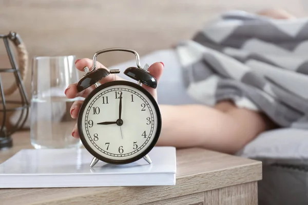 Sleepy woman turning off alarm clock in morning