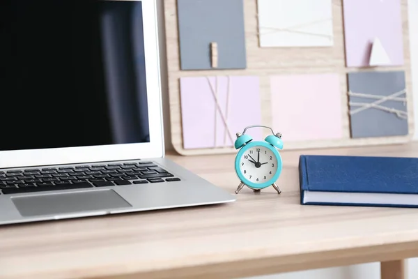 Laptop and alarm clock on table