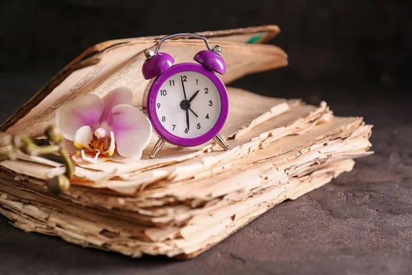Old book, alarm clock and flower on dark background