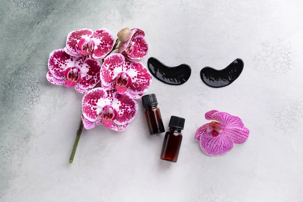 Under-eye patches with essential oil and orchid flowers on light background