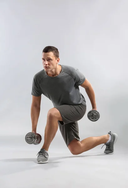 Sporty young man training with dumbbells against grey background — Stock Photo, Image