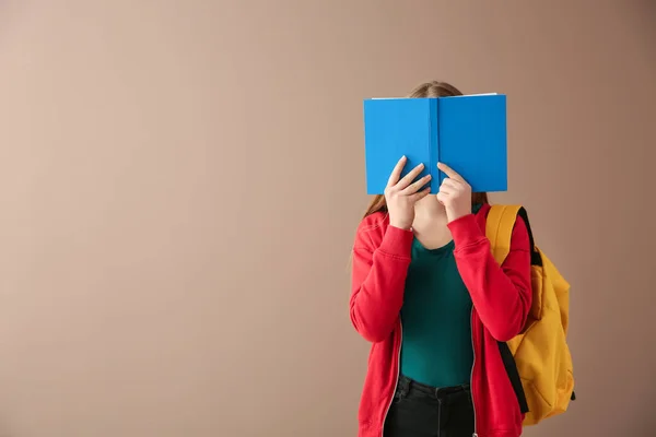 Schoolgirl with book on color background — Stock Photo, Image