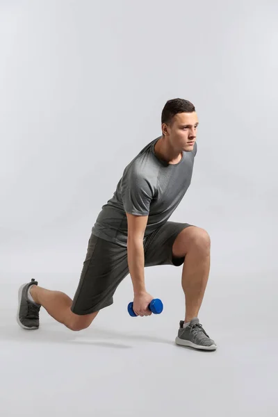Sporty young man training with dumbbells against grey background — Stock Photo, Image