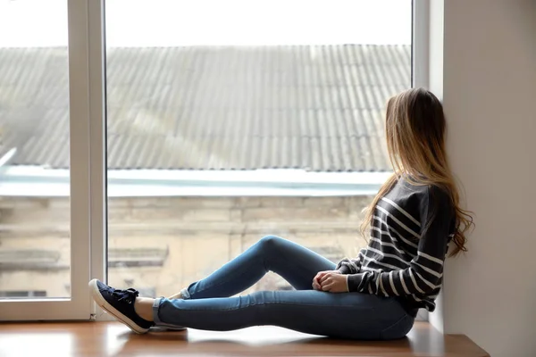 Beautiful young woman sitting on window sill — Stock Photo, Image