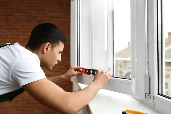 Молодой рабочий ремонтирует окна в квартире — стоковое фото