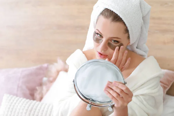 Jeune femme avec des patchs sous les yeux regardant dans le miroir à la maison — Photo