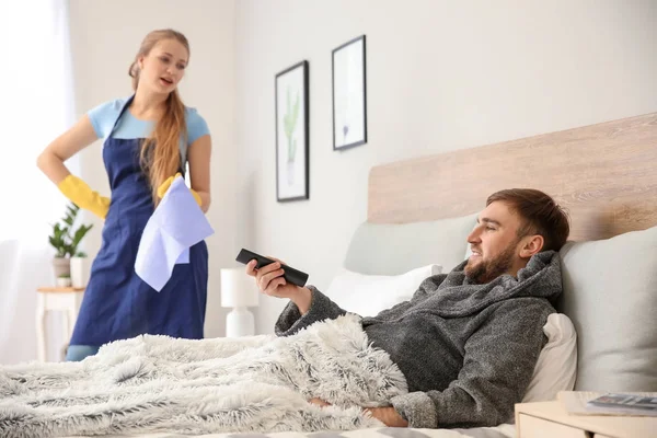Leniwy Mąż ogląda telewizję, a jego żona oburzony Robienie prac domowych w domu — Zdjęcie stockowe
