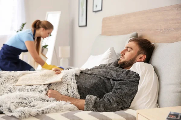 Marido perezoso acostado en la cama mientras su esposa haciendo tareas en casa — Foto de Stock