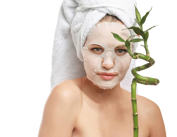 Beautiful young woman with sheet facial mask and bamboo branch on white background — Stock Photo, Image