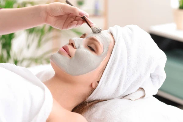 Cosmetólogo aplicación de máscara en la cara de la mujer joven en el salón de belleza — Foto de Stock