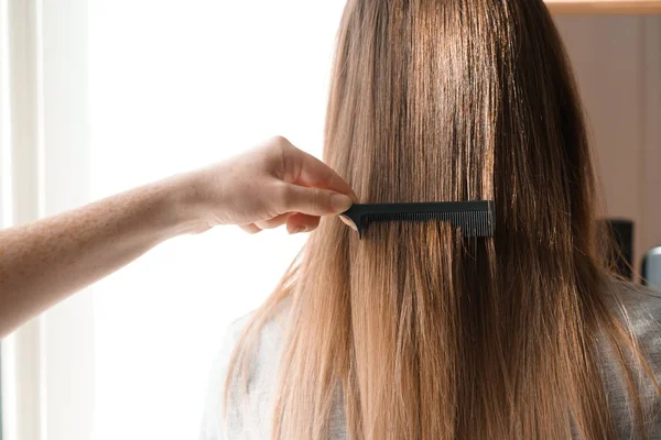Парикмахер расчесывает длинные волосы молодой женщины в салоне — стоковое фото