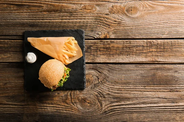 Slate plate with tasty burger and french fries on wooden background — Stock Photo, Image