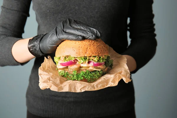 Mujer con sabrosa hamburguesa sobre fondo gris — Foto de Stock