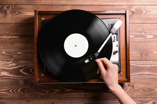 Woman switching on record player with vinyl disc on wooden background — Stock Photo, Image