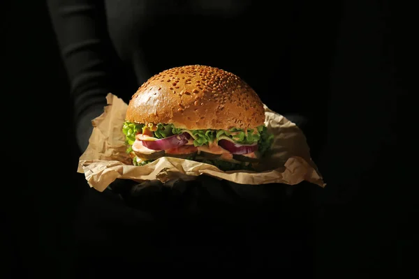 Mujer con sabrosa hamburguesa sobre fondo oscuro — Foto de Stock