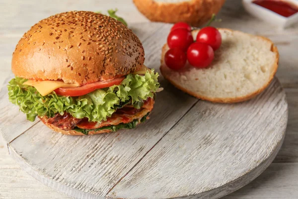 Tasty burger, bun and tomato on wooden board — Stock Photo, Image