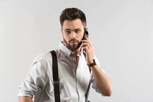 Fashionable young man talking by phone on light background — Stock Photo, Image