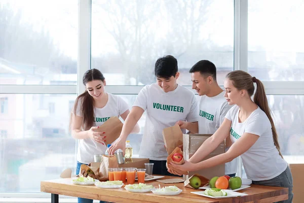 Young volunteers with food for poor people indoors — Stock Photo, Image